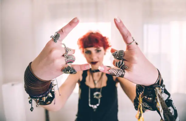 Young red haired woman dressed in rock and heavy metal style raising her hands and showing devil horns gesture