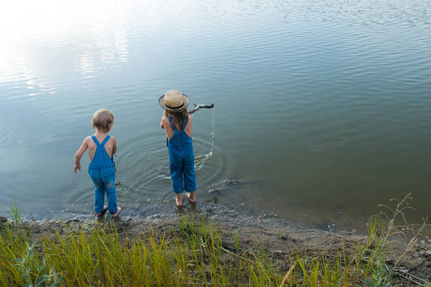 Two boy friends are sitting on a wooden bridge and fishing. Children on a fishing trip.