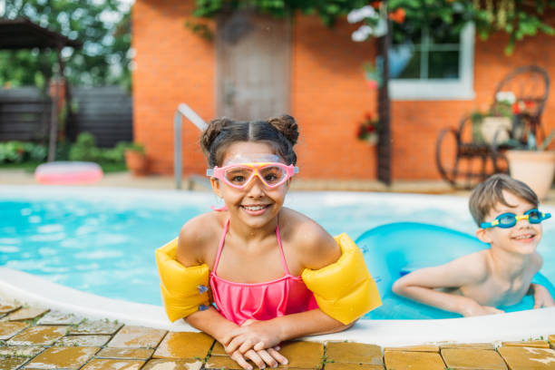 portrait of little siblings swimming in swimming pool together on summer day - inflatable ring water wings swimming pool float imagens e fotografias de stock