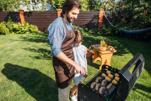 istock son looking at father cooking sausages and corn on grill on backyard 1008570578