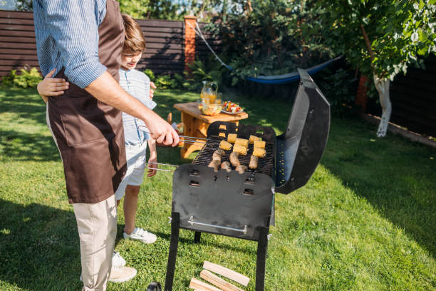 istock partial view of son looking at father cooking sausages and corn on barbecue on backyard 1008570624