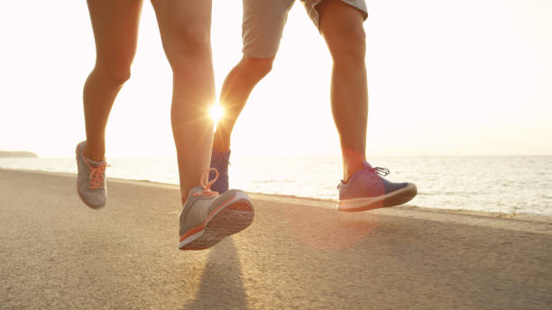 istock LOW ANGLE, SUN FLARE: Fit couple runs down sunny asphalt ocean road in summer. 1008573290