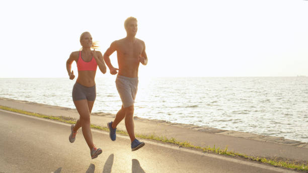 istock Smiling Caucasian couple illuminated by summer sun runs along empty ocean road. 1008573334