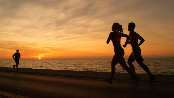 istock SILHOUETTE: Orange sun rays illuminate athletic man and woman on evening jog. 1008573394