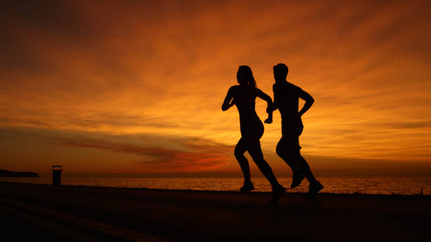 istock SILHOUETTE: Unknown athletic couple running along calm ocean at orange sunset. 1008573416