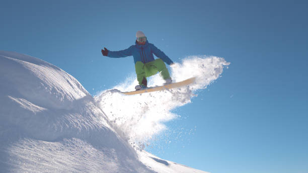 istock CLOSE UP: Pro snowboarder jumping in fresh snow, spraying snowflakes over sun 1008573448