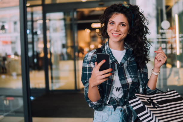 istock Happy woman with mobile phone exiting shopping mall 1008633708