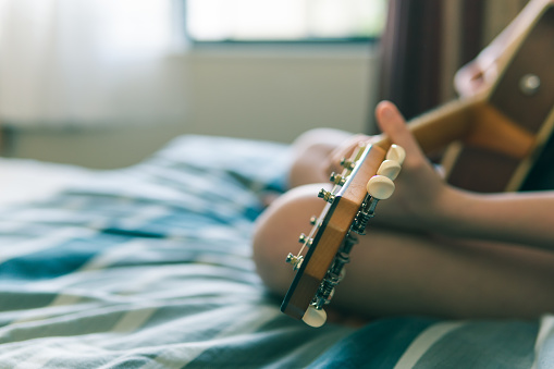 An anonymous, sige-angled view of a girl playing a guitar while sitting on a bed