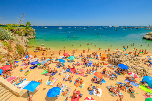 Cascais, Portugal - August 6, 2017: people sunbathing on Praia da Rainha, a small beach sheltered by cliffs in center of Cascais, Lisbon Coast, Portugal. Turquoise sea and blue sky. Summer holidays.