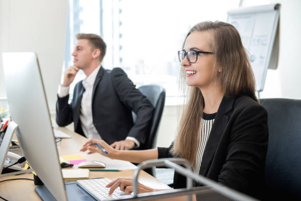 Happy businesswoman working with computer in the office Smiling happy businesswoman white collar worker concentrating on working with desktop computer in the office junior level stock pictures, royalty-free photos & images