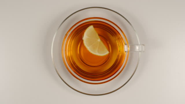 TOP VIEW: Lemon slice swims in a black tea in a glass tea cup with a dish