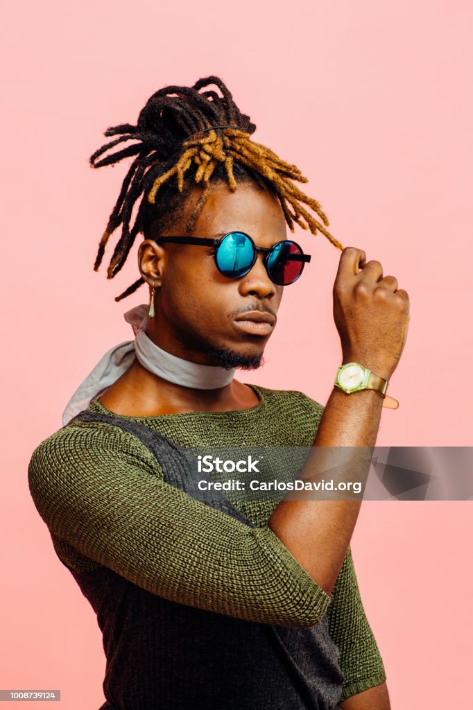 Portrait of a young man in green with dreadlocks and blue sunglasses Portrait of a young man in green with dreadlocks and blue sunglasses, isolated on pink Men Stock Photo