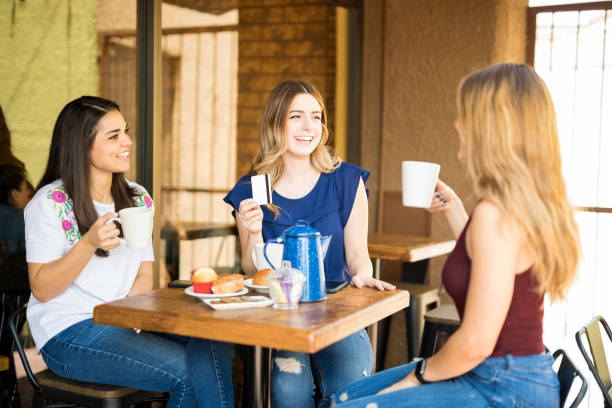 Group of girls having coffee and gossiping at restaurant, with one women holding credit card for payment.