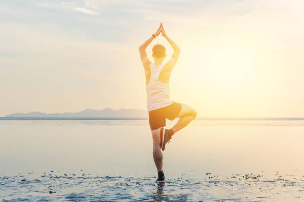 istock Young asian man doing yoga exercise at sunset beach 1008765440