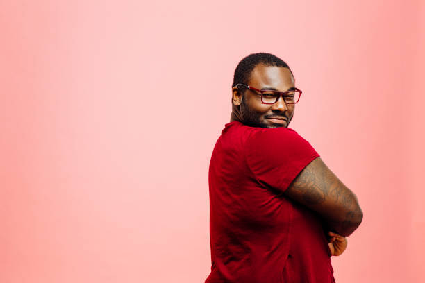 Portrait of a plus size man in red shirt and glasses looking back at camera Portrait of a plus size man in red shirt and glasses looking back at camera, isolated on pink background smirking stock pictures, royalty-free photos & images