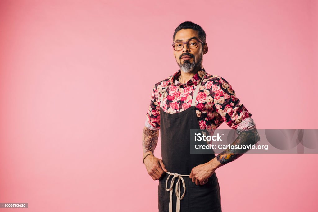 Portrait of a cool cook with tattoos with hands on waist Portrait of a stylish cook with tattoos with hands on waist, isolated on pink studio background Chef Stock Photo