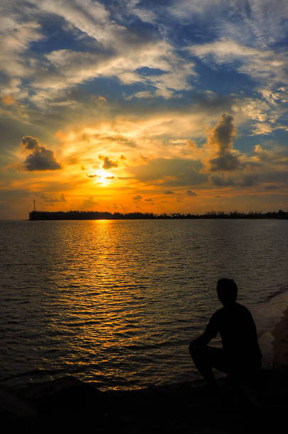 istock Silhouettes of single men sitting lonely on the beach 1008819002