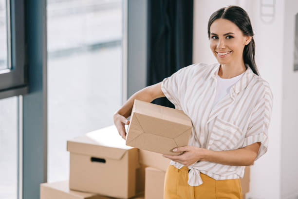 istock happy young woman holding box and smiling at camera during relocation 1008844938