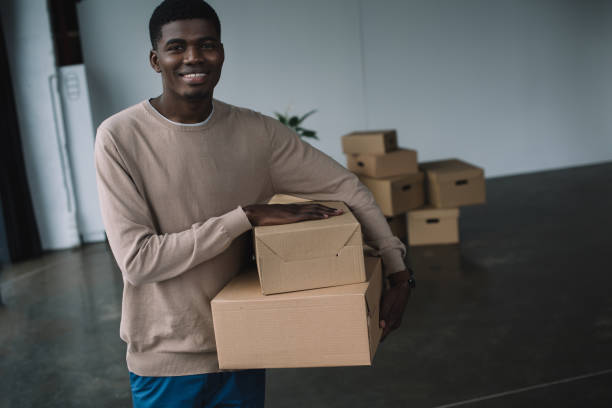 istock young african american man holding boxes and smiling at camera while relocating in new office 1008845106