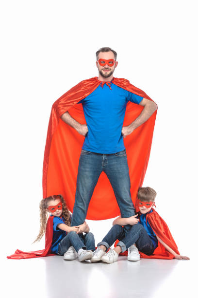 super dad standing with hands on waist and looking at camera while kids hugging his legs isolated on white super dad standing with hands on waist and looking at camera while kids hugging his legs isolated on white superhero photos stock pictures, royalty-free photos & images
