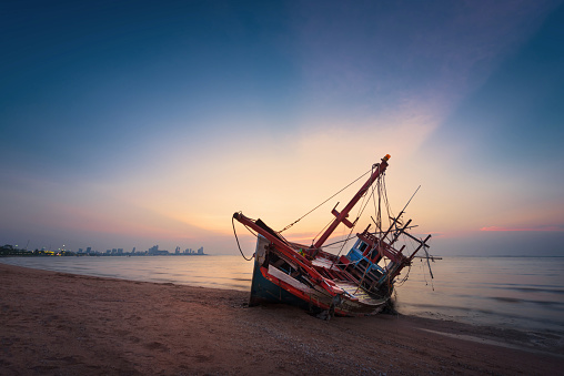 Abandoned shipwreck of wood fishing boat on beach at twilight time