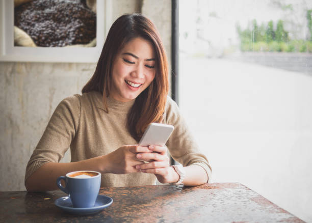 asiática hermosa mujer joven con teléfono inteligente para los negocios, compras en línea, transferencia financiera, banca por internet dinero,. en la cafetería café sobre fondo borroso. - restaurant sitting adult beauty fotografías e imágenes de stock