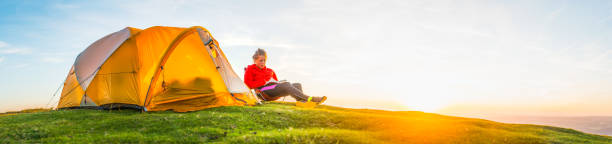 istock Young woman reading book camping on idyllic mountain sunset panorama 1008876126