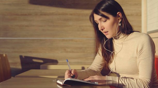 istock Young woman sitting in cafe with headphones and making notes in notebook 1008880090