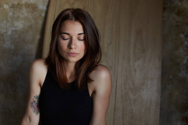 istock Young attractive tender female model enjoys loneliness, spending time alone indoors, closing eyes, have rest, enjoys silence over wooden and concrete wall. Human beauty, care and health concept. 1008898312