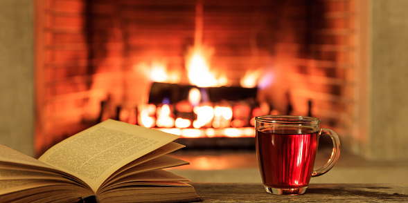 Relaxation at home. Close up of a cup of tea and a book on a burning fireplace background