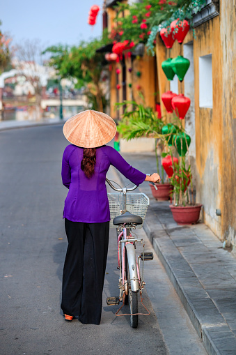 Vietnamese woman with a bicycle in old town in Hoi An city, Vietnam. Hoi An is situated on the east coast of Vietnam. Its old town is a UNESCO World Heritage Site because of its historical buildings.