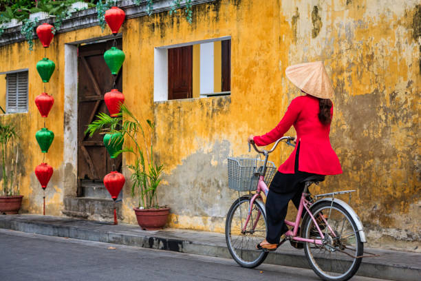 Vietnamese woman riding a bicycle, old town in Hoi An city, Vietnam Vietnamese woman riding a bicycle in old town in Hoi An city, Vietnam. Hoi An is situated on the east coast of Vietnam. Its old town is a UNESCO World Heritage Site because of its historical buildings. hoi an stock pictures, royalty-free photos & images