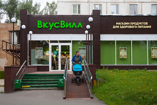 MOSCOW, RUSSIA - JULY 24, 2018: Vkusvill food store building and woman with baby stroller in Muranovskaya street. This street is located in Bibirevo district of Moscow.