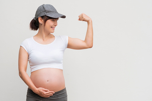 Beautiful pregnant Asian woman showing her bicep on white background