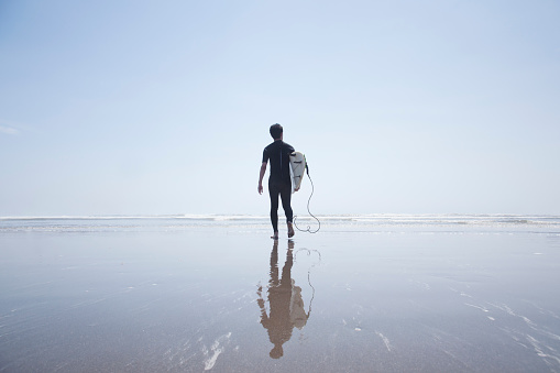 Japanese male surfer wearing a wet suit walking on the shore.
