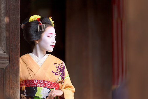 Kyoto, Japan - November 28, 2015: A woman in traditional Maiko dress looks out from a doorway. Many tourists visiting Kyoto will pay to have the Maiko and Geisha makeover experience.