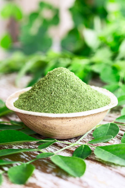 Moringa powder (Moringa Oleifera) in coconut bowl with original fresh Moringa leaves on wooden background Moringa powder (Moringa Oleifera) in coconut bowl with original fresh Moringa leaves on wooden background. Healthy product, superfood, vitamin. Vertical schot. moringa leaves stock pictures, royalty-free photos & images