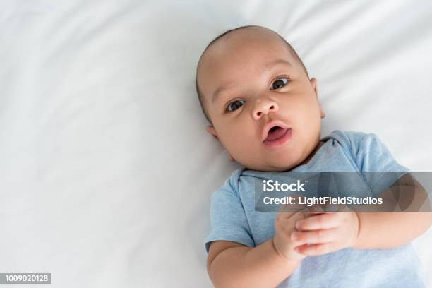 Infant Little Baby With Surprised Expression Looking At Camera While Lying In Bed Stock Photo - Download Image Now