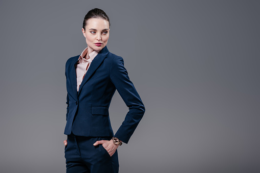attractive adult businesswoman with hands in pockets looking away isolated on grey