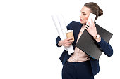 overworked adult businesswoman with lot of paperwork and coffee to go talking by phone isolated on white