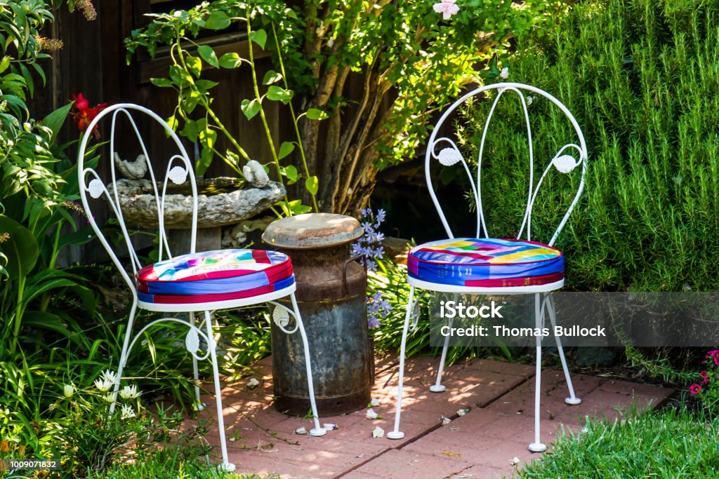 Two Ice Cream Chairs In Garden Two Ice Cream Chairs, Milk Can And Birdbath In Garden Corner Birdbath Stock Photo
