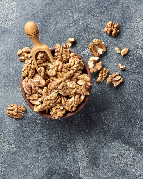 istock Walnut kernels with wooden scoop on gray background with copy space. Nuts in clay bowl. Top view. 1009079574