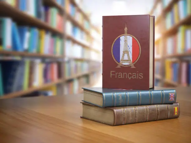 Photo of Learn French concept. French dictionary book or textbok with flag of France and Eiffel tower on the cover in the library.