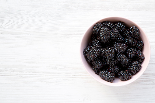 Top view, fresh organic blackberries in pink bowl on a white wooden background. Closeup. Copy space.