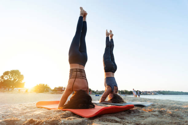 deux jeunes femmes exerçant sur la plage - inversion yoga photos et images de collection