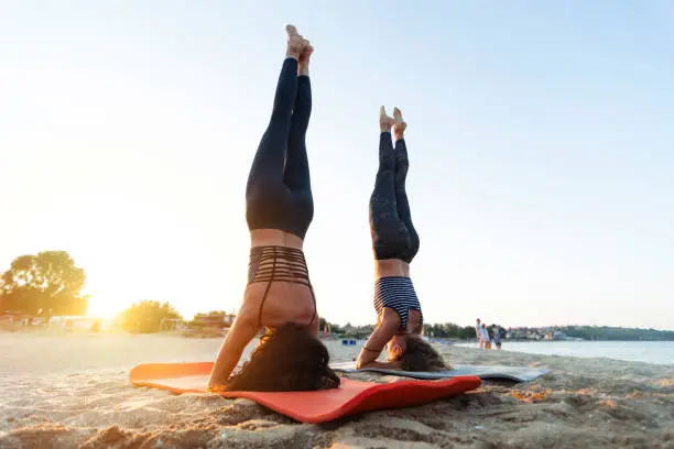 Two young women doing yoga outdoor on the beach in sunset time