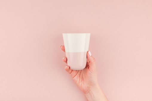 Creative image of woman hand holding coffee cup with copy space on millennial pink background in minimalism style. Concept template for feminine blog, social media