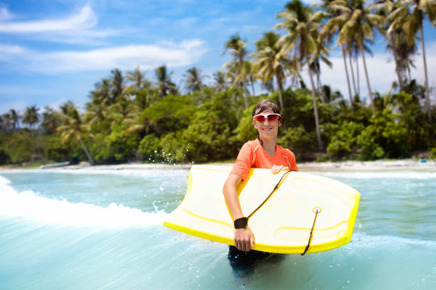 istock Child surfing on tropical beach. Surfer in ocean. 1009213436