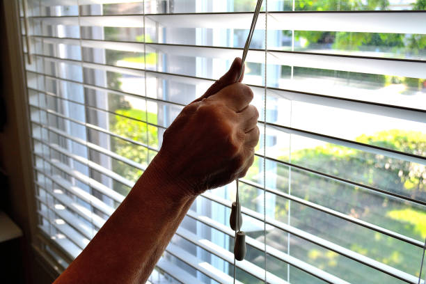 Lifestyle. " Closing or Opening a Window Shade " Lifestyle...This close up shot, shows an arm lowering or opening a bedroom window shade. dark window blinds stock pictures, royalty-free photos & images