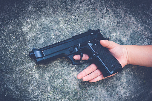 Gun in the hands of a children on a gray background.